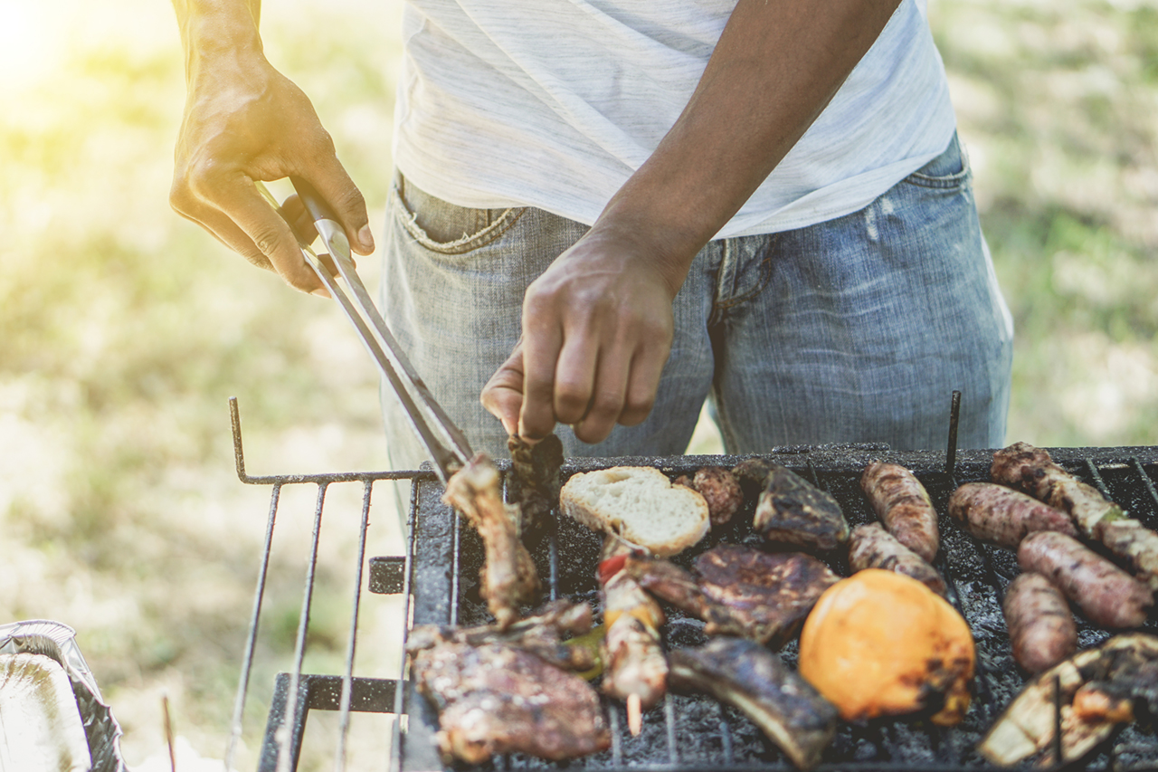 man-cooking-meat-on-barbecue-chef-putting-some-sausages-on-grill-in-park-outdoor