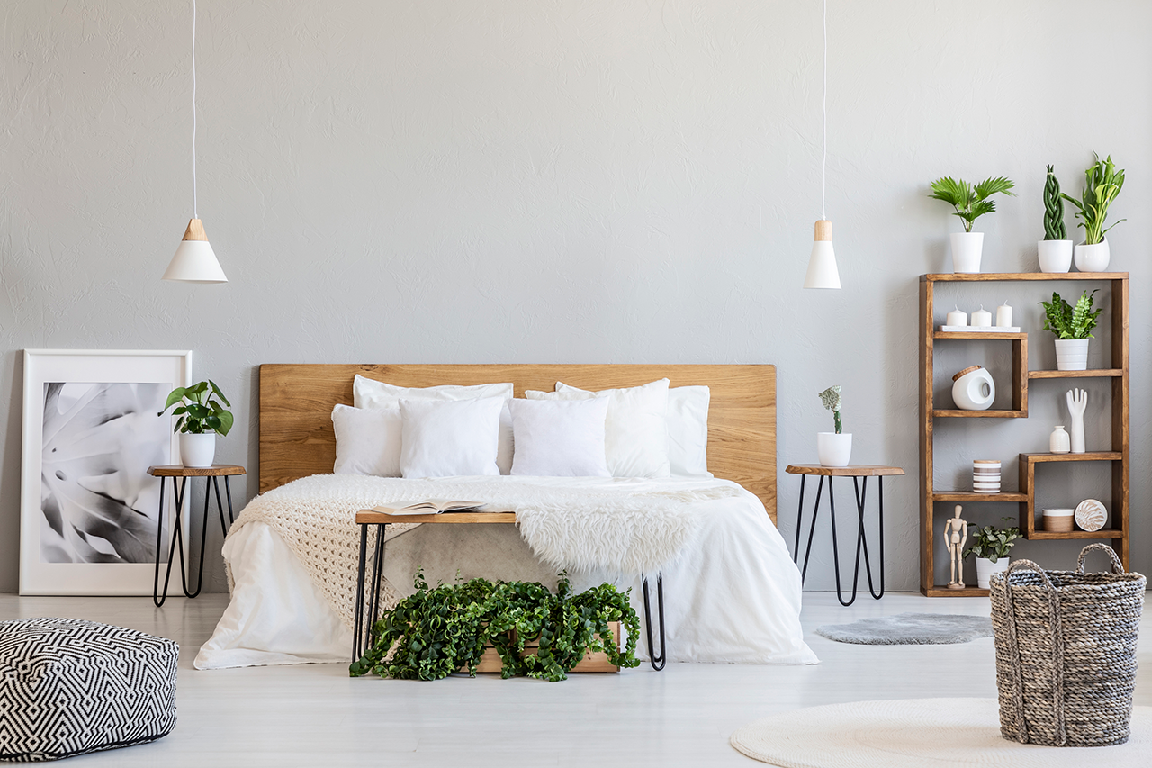 Patterned pouf and basket in bright bedroom interior with lamps, plants, and poster next to bed